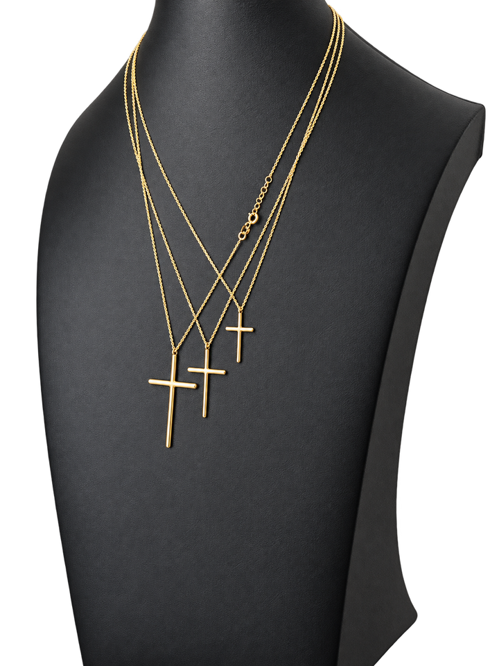 Three sizes of solid 10K gold cross pendant necklaces on a black jewelry display — angled view