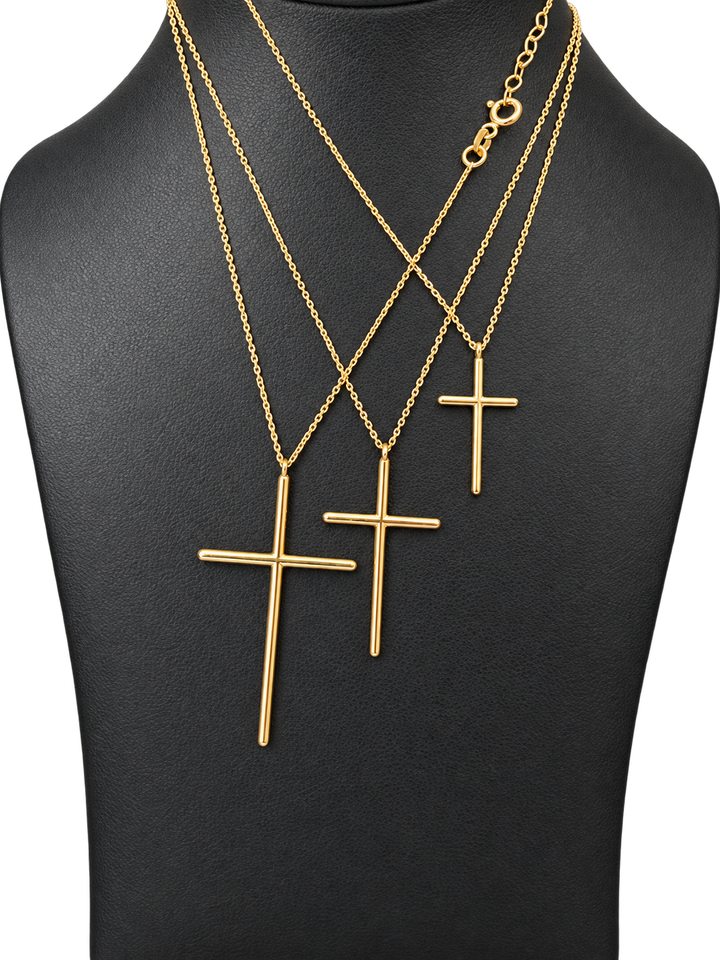 Three sizes of solid 10K gold cross pendant necklaces on a black jewelry display — close-up