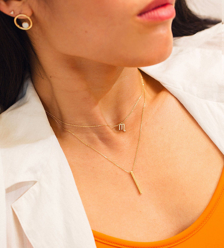woman wearing layered necklaces featuring a 14K gold bar pendant necklace with delicate chain styling