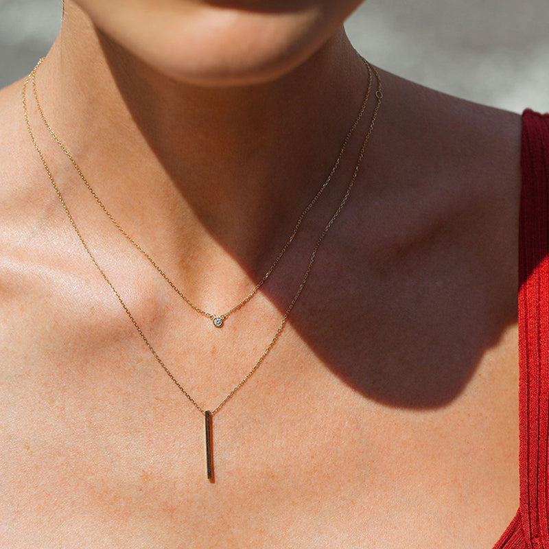 layered 14K gold bar pendant necklace on model with delicate chains and small round accent