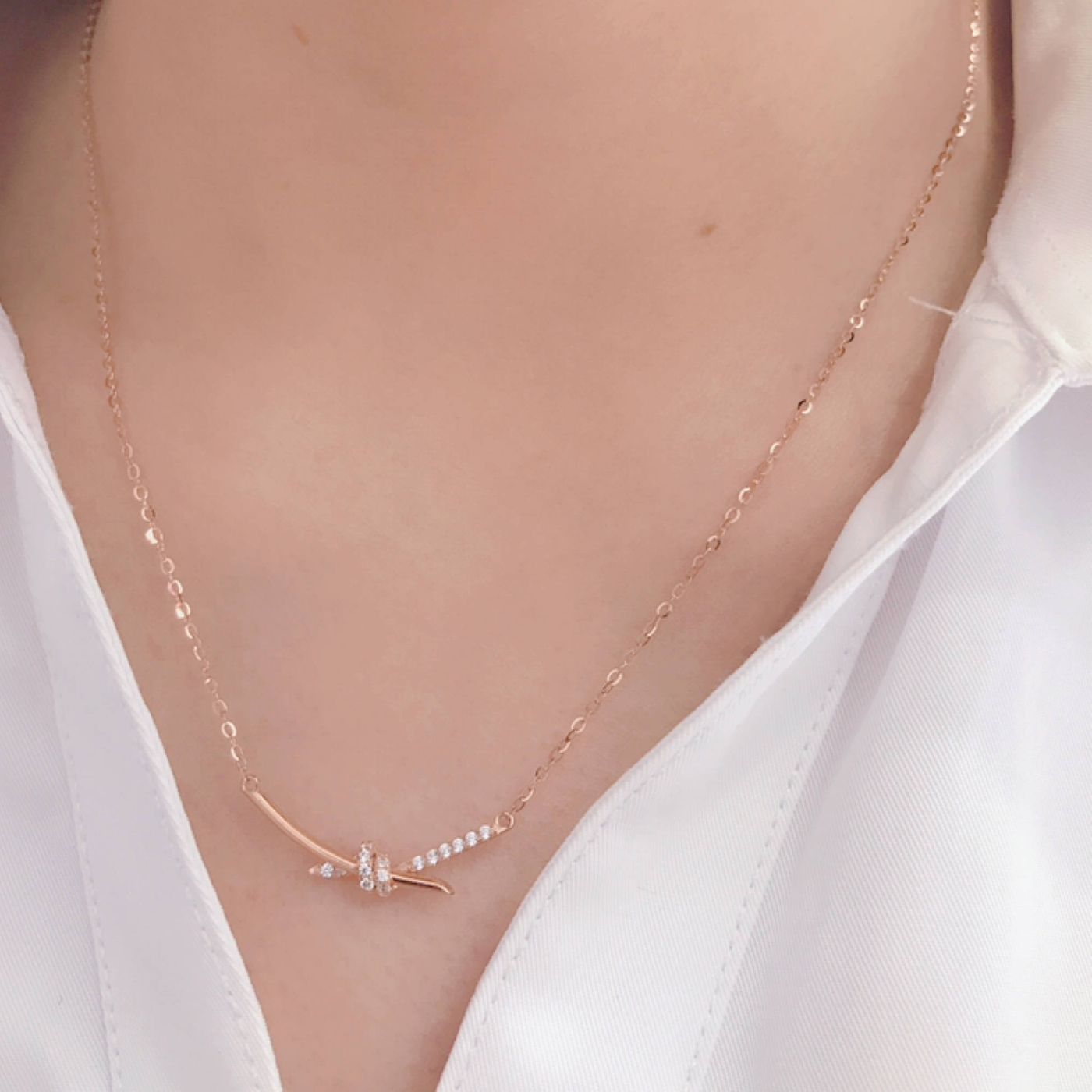 14K gold diamond knot necklace worn on model with white blouse delicate chain and curved bar